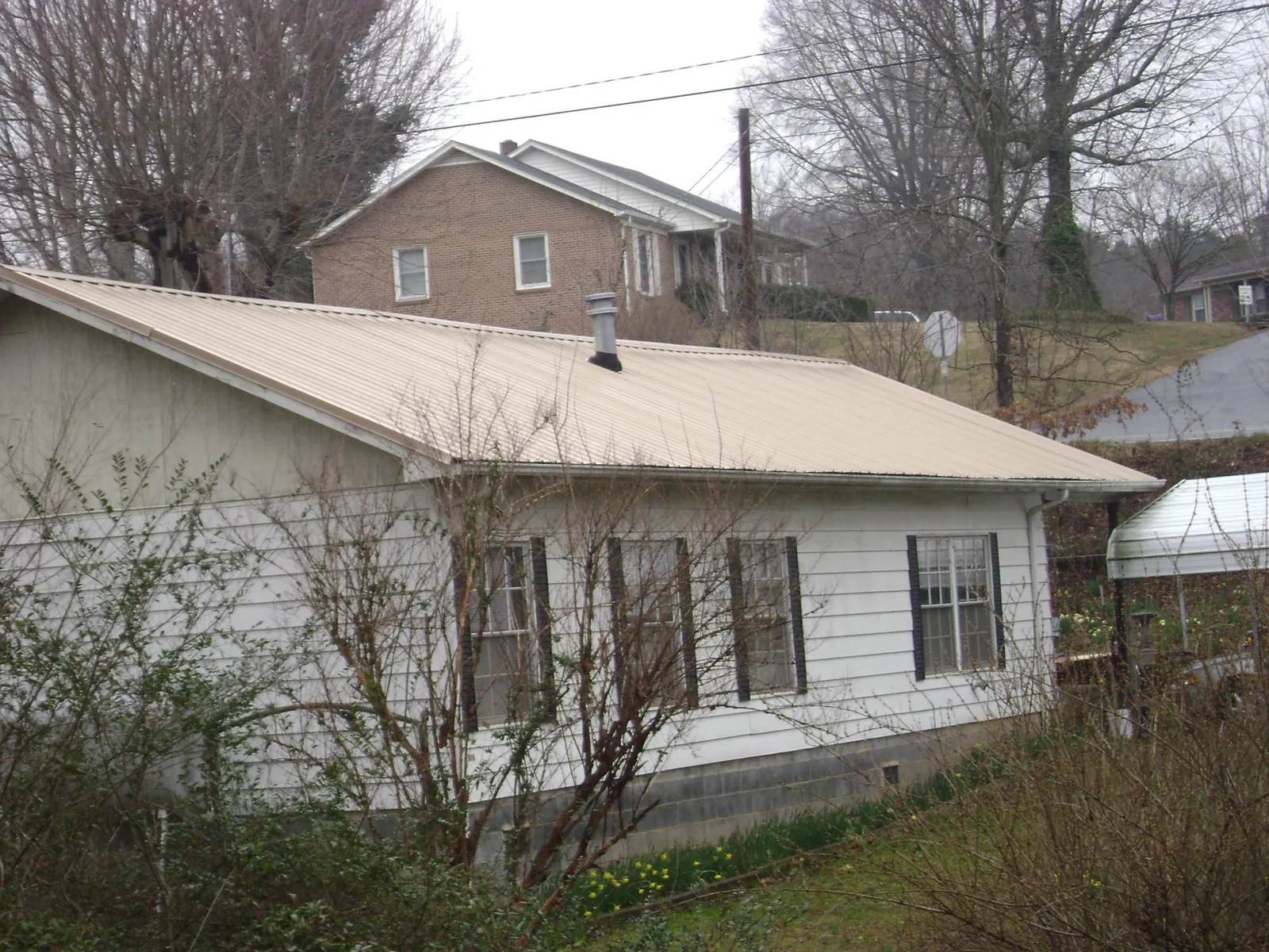 Tan metal roof on a white sided house set into a hillside — Commercial Roofing by Roofing Brothers in Atlantic Beach