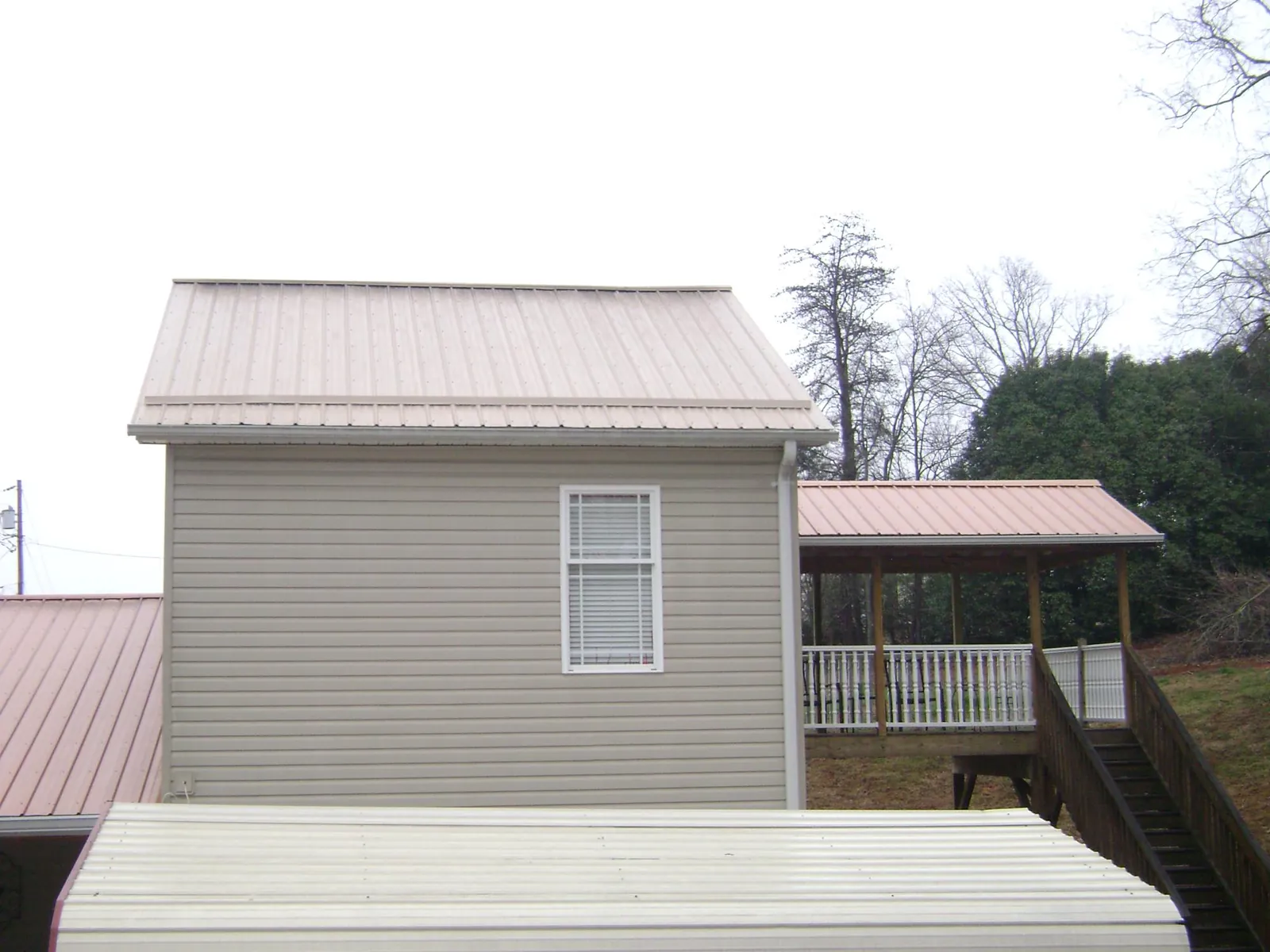 Tan metal roofs on a two story addition and attached porch, from a Roof Replacement job in Atlantic Beach